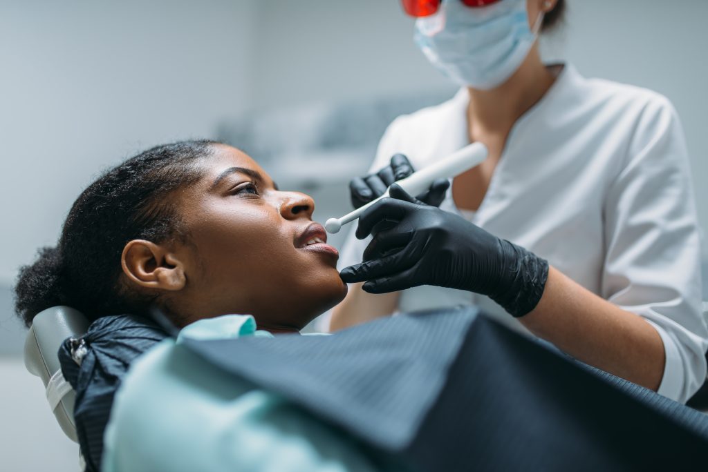 Dentist installs the seal on the tooth, woman in dental clinic. Female patient in dentistry cabinet, stomatology