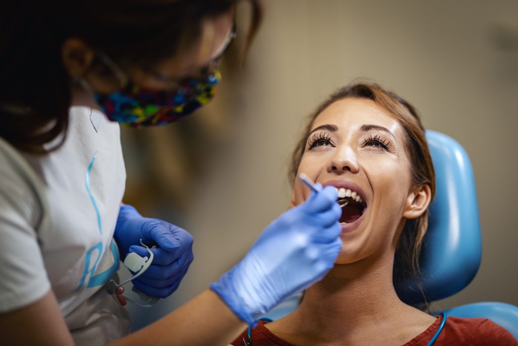 The beautiful young woman is at the dentist. She sits in the dentist's chair and the dentist checkup her teeth.