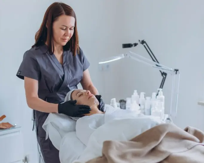 Aesthetician doing facial services on woman lying down on bed